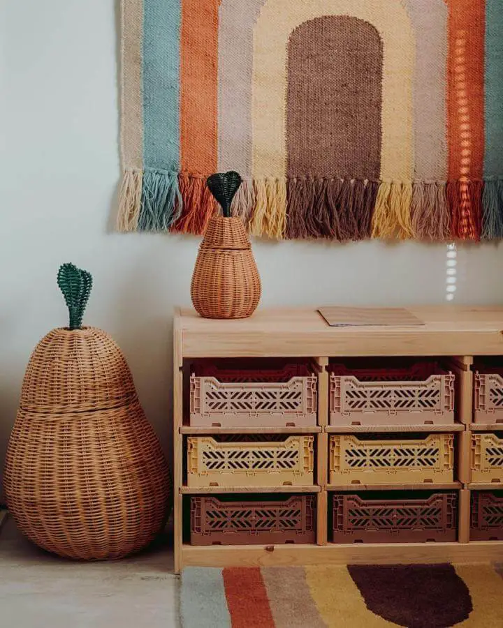 Natural wicker baskets and pastel crates in a wooden storage shelf with colorful woven wall hanging in a playroom from @viivivalokainen.