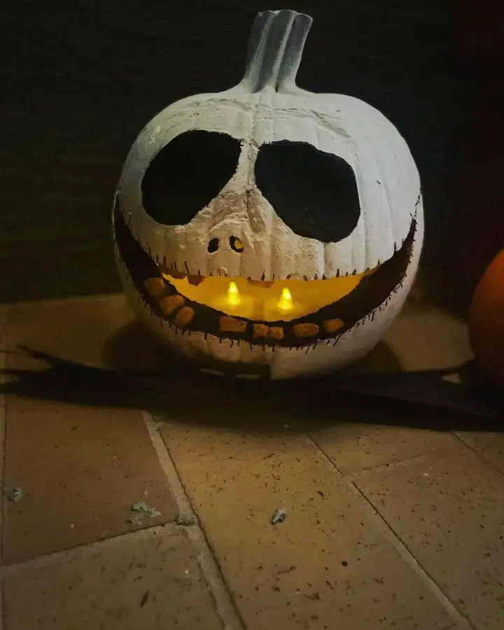 White painted pumpkin from @tullelegomasterbuilders. Features black painted face with battery-powered yellow lights inside.