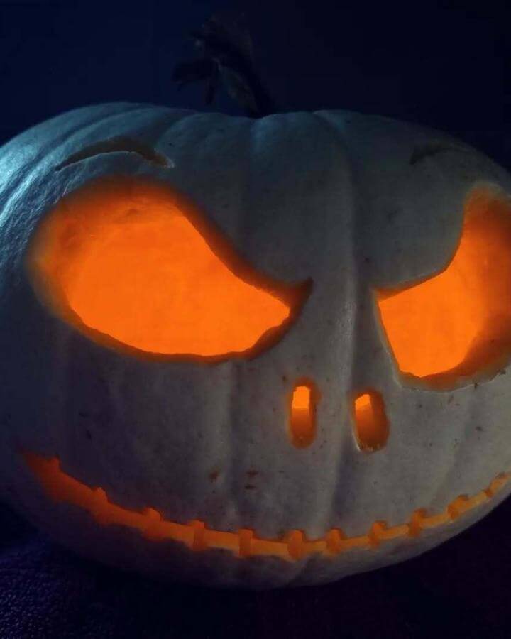 White carved pumpkin from @pdbaldry. Glowing orange light illuminates skellington-style face design.