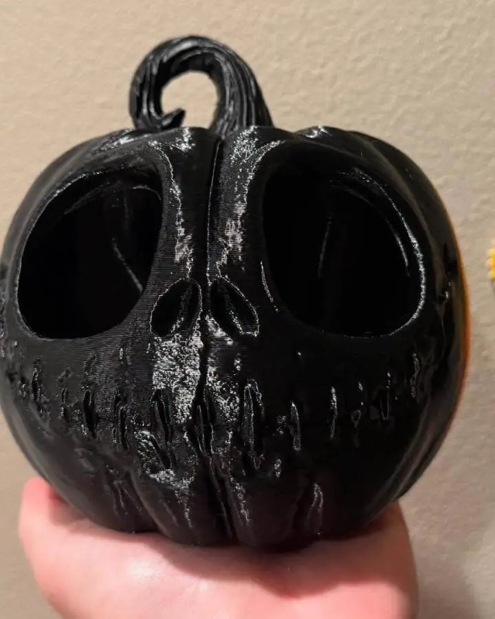 Glossy black 3D printed jack skellington pumpkin decoration from @slightlysulliedcreations held in someone's hand.