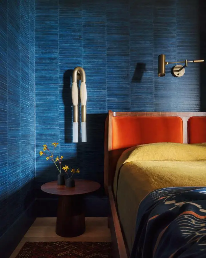 Deep blue textured bedroom from @suzannasantostefanodesign with orange leather headboard and brass lighting fixtures.
