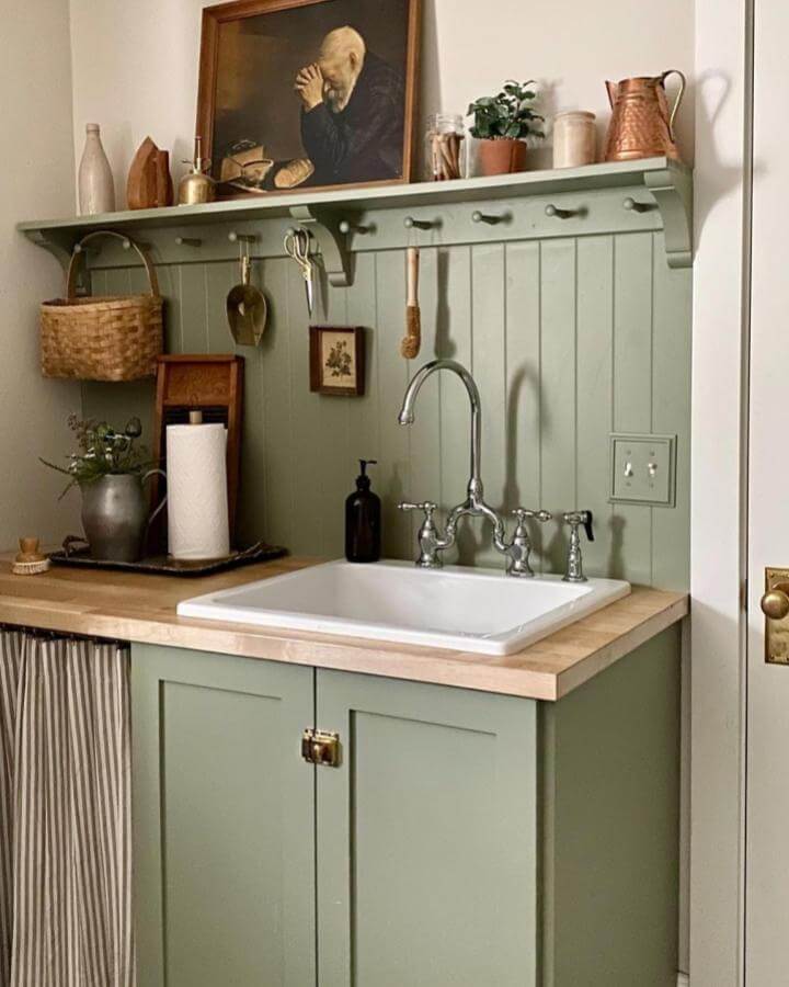 Sage green vintage farmhouse laundry sink ideas with wood countertop and beadboard backsplash from @ciarakenaston. Cozy functional setup with rustic accents.