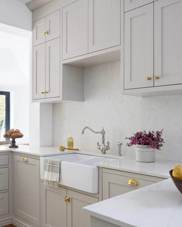 White ceramic farmhouse sink with soft gray cabinets and brass hardware by @fausettinteriors in a bright laundry space.
