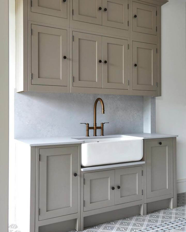 White farmhouse sink with brushed brass faucet and taupe cabinetry in a laundry space from @bakehouse_ltd. Classic yet fresh setup.