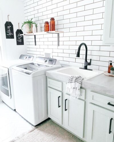Matte black faucet and white farmhouse sink in a clean laundry room with subway tile and warm rustic accents from @farmhouseish