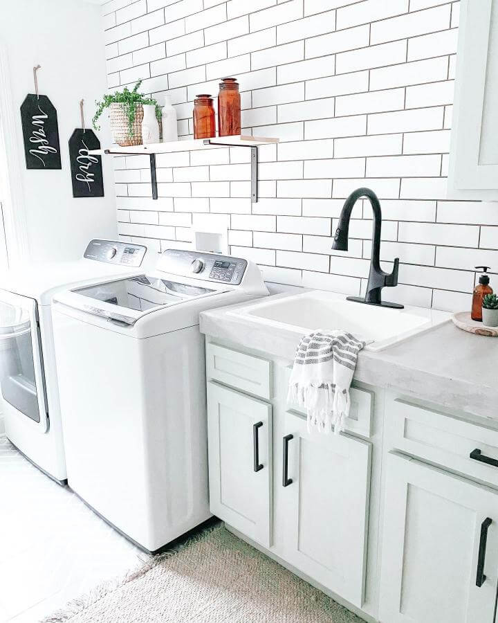 Matte black faucet and white farmhouse sink in a clean laundry room with subway tile and warm rustic accents from @farmhouseish