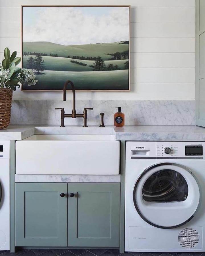 Farmhouse style laundry sink with bronze faucet, sage green cabinetry, marble counter, and landscape artwork by @corinneborio.realtor.