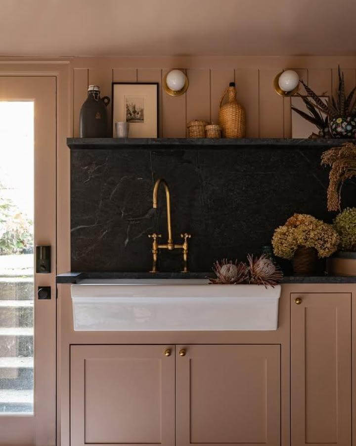 White farmhouse sink with black marble backsplash and brass fixtures laundry space by @jessicanelsondesign for a stylish contrast.