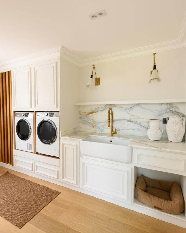 White marble backsplash laundry room sink ideas from @handmadekitchenco with gold faucet and farmhouse sink in bright laundry room.