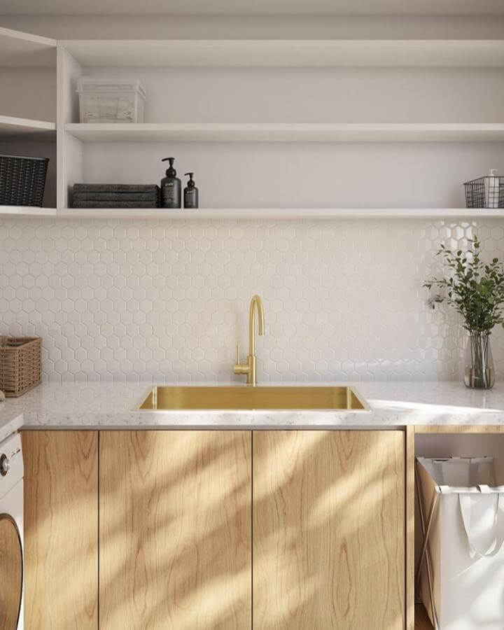 Golden brass sink nestled in a white hex tile backsplash laundry area with wood cabinets and open shelves from @buildmat bright and stylish design