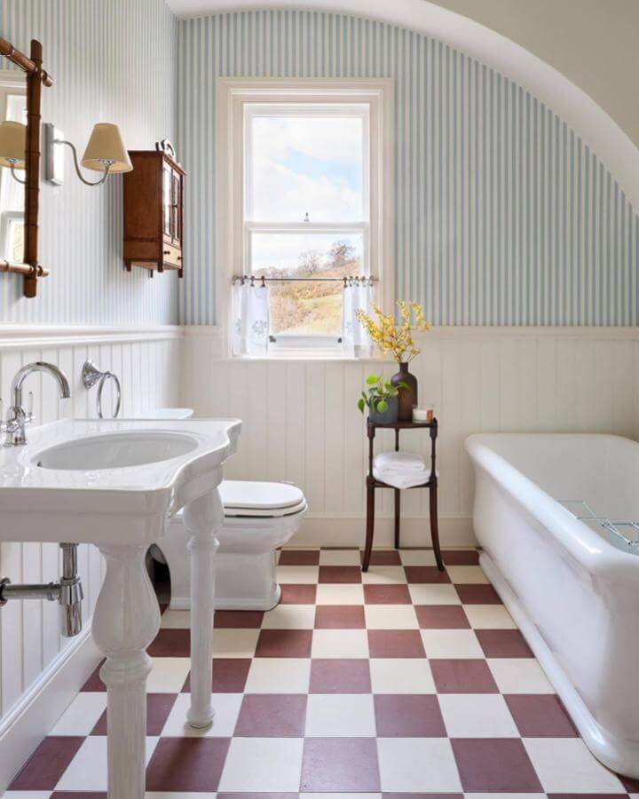 Light blue bathroom ideas with striped wallpaper and classic white wainscoting from @farrowandball, featuring vintage checkered floor and natural light.