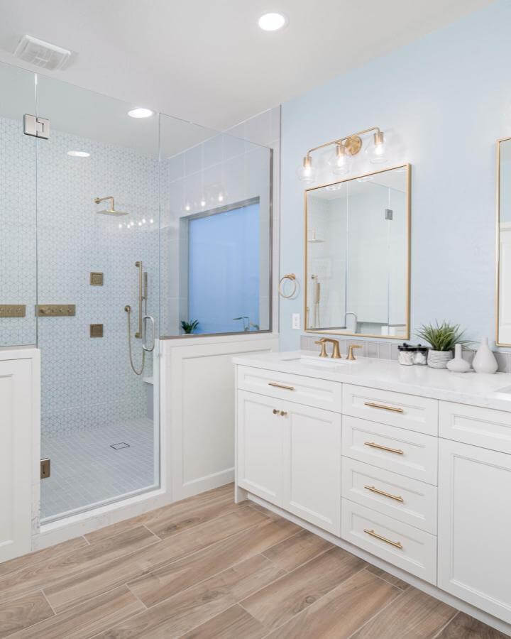 Light blue bathroom ideas featuring light blue walls, brass fixtures, white cabinetry, and wood-look floor from @ikinteriorsllc bright and stylish bathroom
