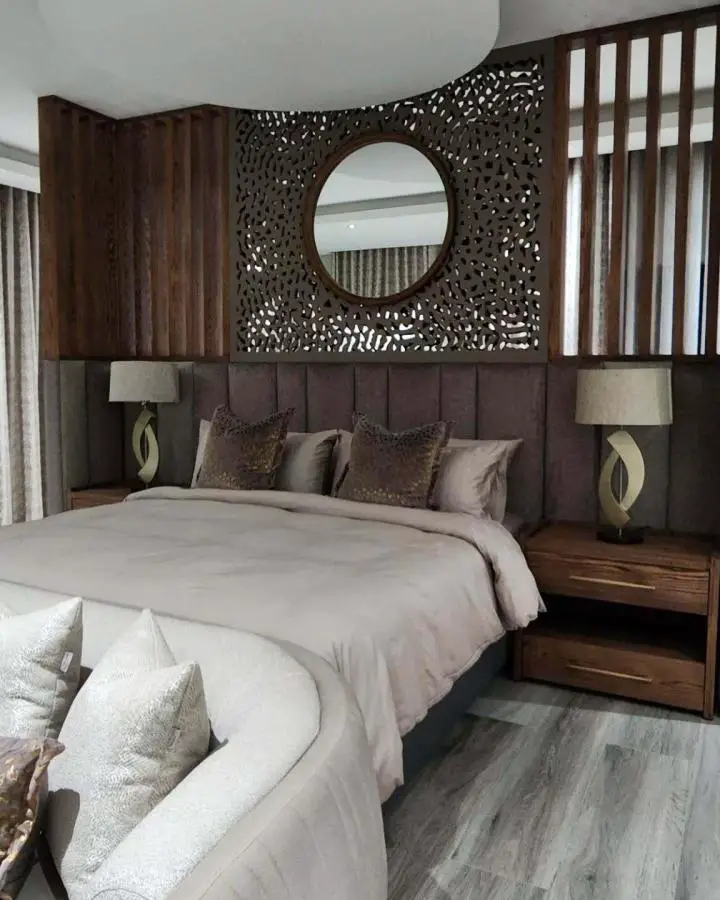 Intricate laser-cut wooden accent wall from @renthea_house_of_interiors showcasing luxurious master bedroom ideas with warm walnut tones.