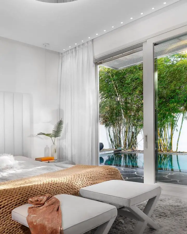Contemporary bedroom with floor-to-ceiling windows from @sallychaprak. Overlooks tropical pool area with natural lighting.