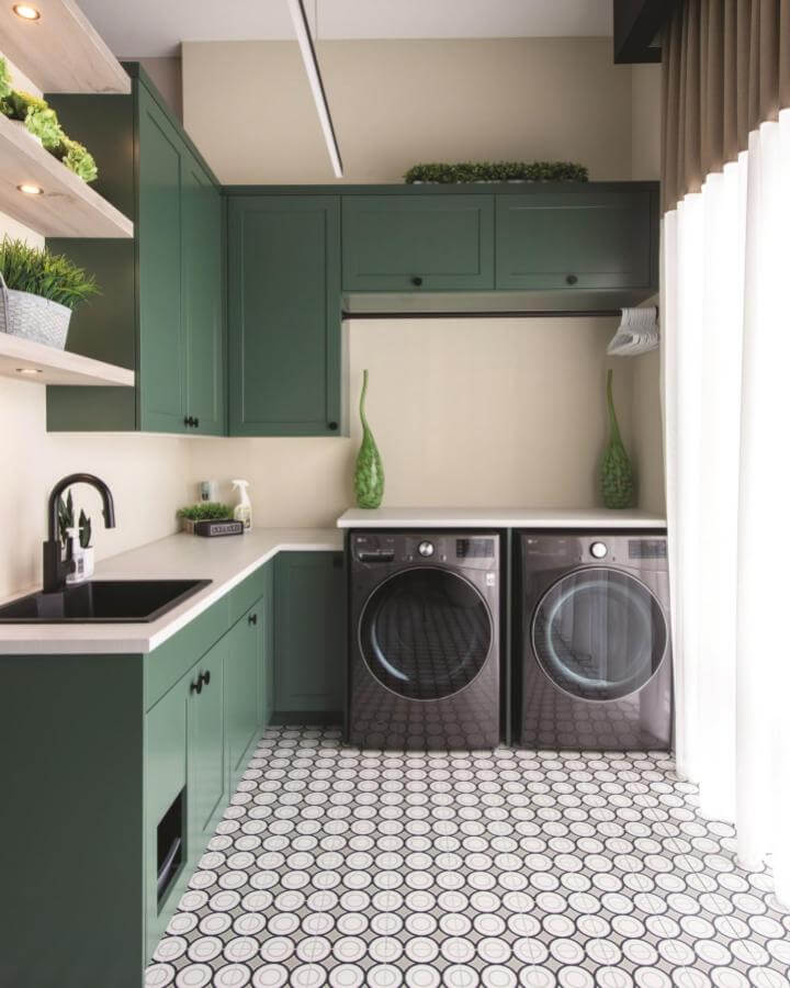 Green Shaker cabinets with black hardware and geometric tile floor in a luxury laundry room by @ourhomesmagazine natural and calming design.