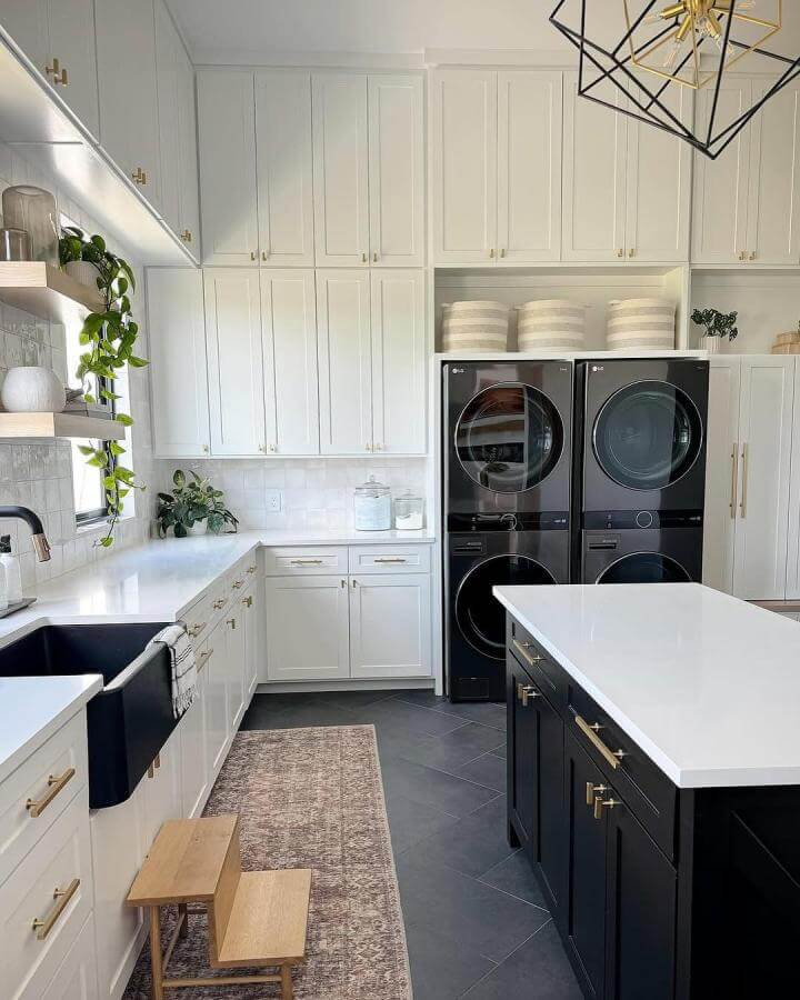 Glossy white and black two-tone cabinets with gold handles in a luxury laundry room from @ashathomeandaway featuring a black farmhouse sink and woven baskets.