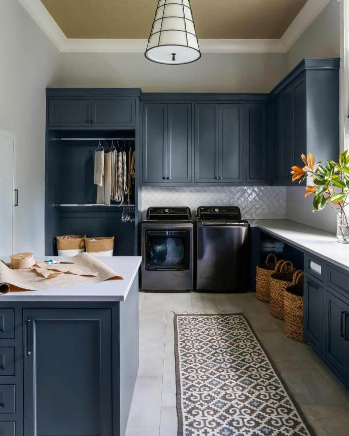 Deep navy cabinetry laundry room from @davispropertiesoftn with patterned rug and woven baskets luxury laundry room ideas