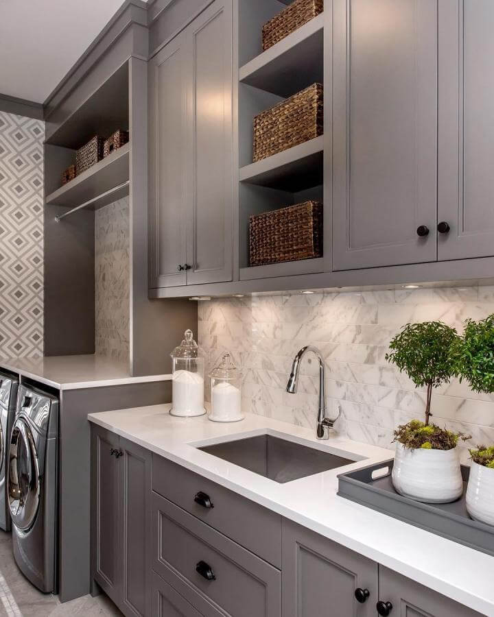 Gray matte cabinetry and white quartz countertop luxury laundry room ideas from @mrcurtiselmy featuring marble backsplash and woven baskets for storage.