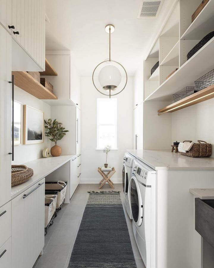 Bright white cabinetry and quartz countertops with wood shelves and black hardware luxury laundry room ideas from @urbanologydesigns. Clean and minimalist with natural accents and a statement light fixture.