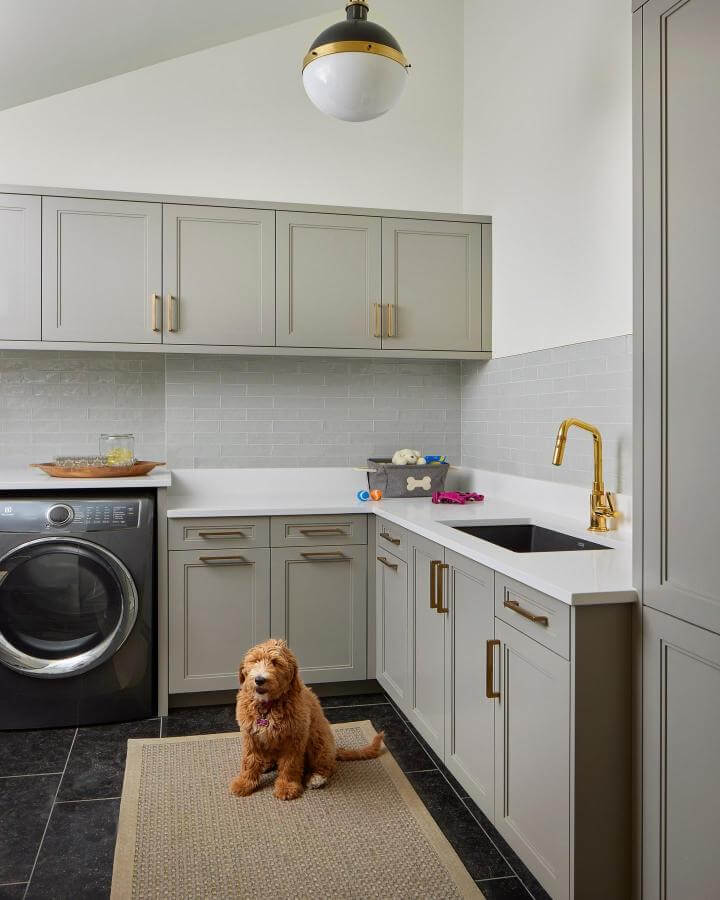Soft gray cabinetry with brass hardware luxury laundry room ideas by @kitchendistributorsinc featuring quartz countertop and gold faucet bright accents.