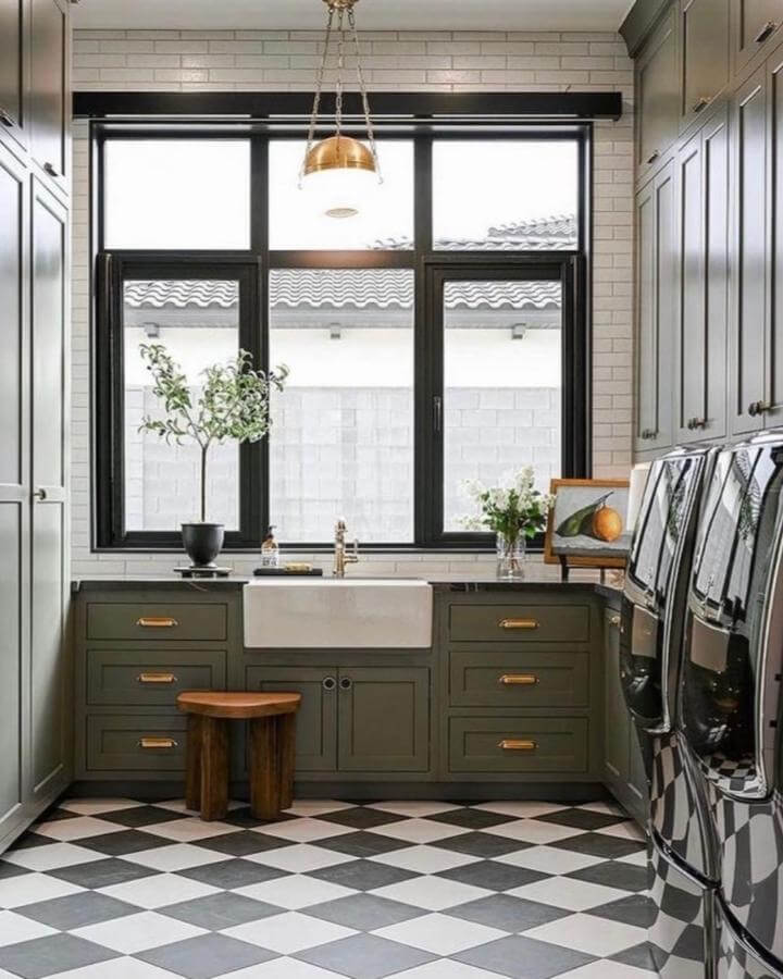Olive green cabinetry and black white checkered tile floor luxury laundry room ideas by @carol_interiors_ with farmhouse sink and brass accents