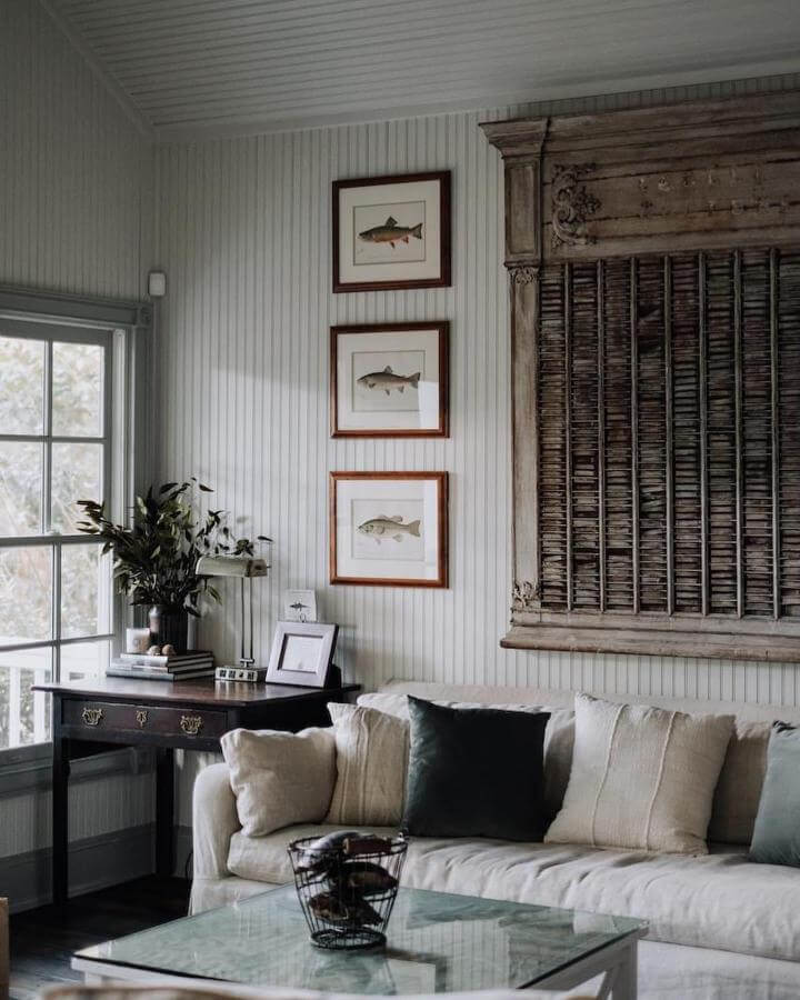 Beige and green coastal living room with vintage wooden shutter and fish print wall art by @kayladevitofineart. Soft natural textures and classic coastal accents bring a fresh, lived-in feel.