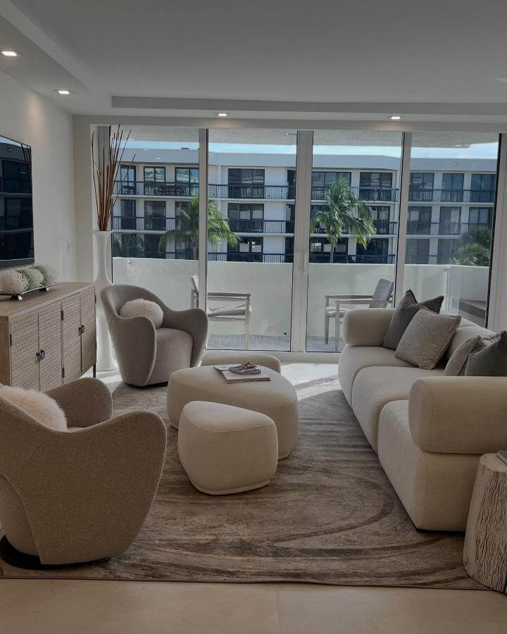 Creamy bouclé chairs and ottoman with natural wood cabinet in a sunlit living room by @chloed_designs showing cozy coastal chic style.