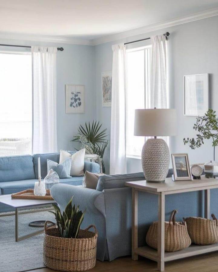 Soft blue upholstered sofas with white curtains and natural wicker baskets by @suzi_yasu. Bright and airy coastal living space with calming blue tones.