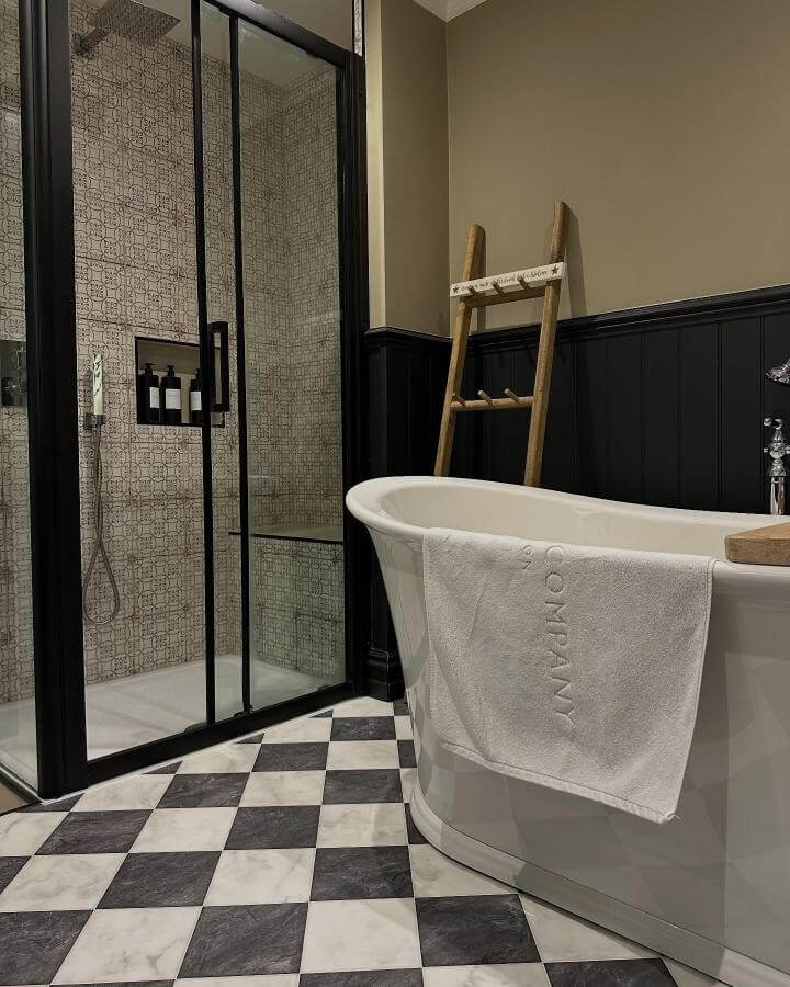 Checkerboard black and white tile floor in moody bathroom with glass shower and wooden towel ladder from @_lifeatdallas, classic yet edgy design.