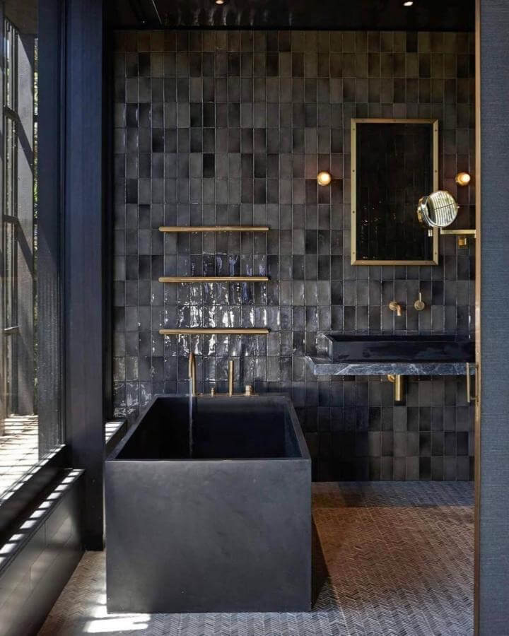 Black glossy tile walls and dark charcoal bathtub with brass accents in a moody bathroom by @cxsdesigns creating a striking, dramatic space.
