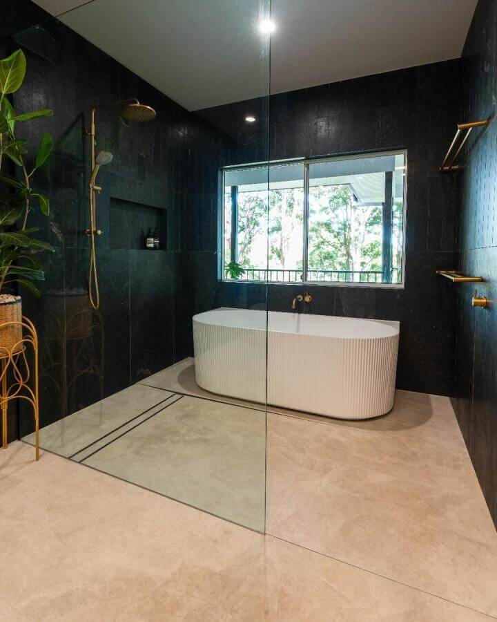 Black tile bathroom walls with white ribbed tub and brass fixtures from @nelsonkahlervisuals. Moody and modern with natural light.