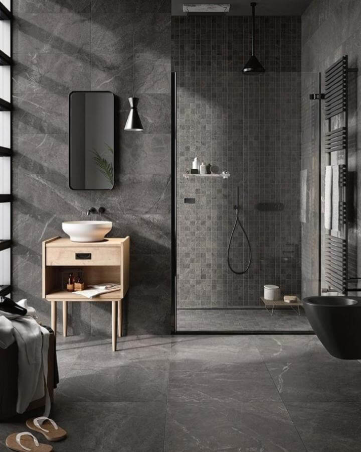 Natural wood vanity and matte black fixtures in a moody bathroom ideas setting with dark gray stone tiles from @idealtileimporting creating warmth and texture.