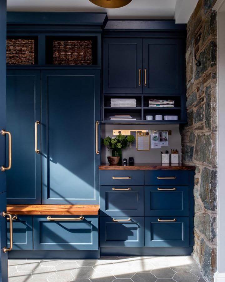 Navy blue cabinetry and warm wood accents with brass hardware for mudroom built ins ideas by @aidandesign creating bold and cozy storage.