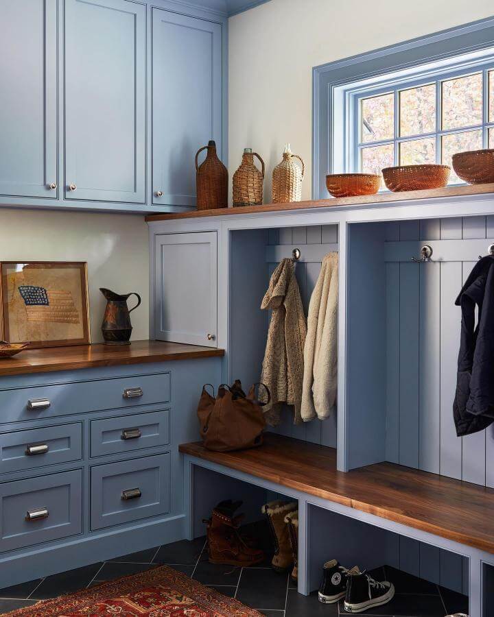 Soft blue shaker cabinetry with warm wood bench and countertop from @cummingsarchitectureinteriors. Functional hooks and cubbies for storage.
