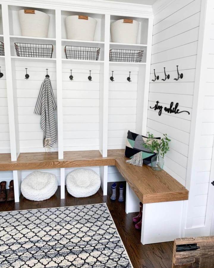 Warm wooden bench mudroom built ins ideas with white shiplap and black hooks from @kristina.roy. Functional and cozy organization space with baskets and pet beds.