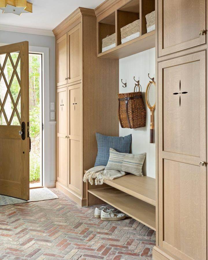 Light oak built-in mudroom bench with black metal hooks and woven baskets by @tiffanyharrisdesign showcasing natural textures and rustic style