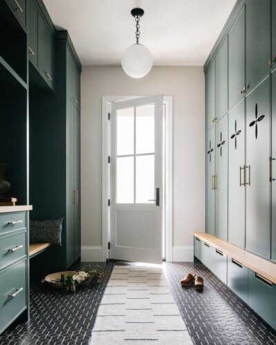 Deep green cabinetry with cutout accents and wood bench tops in a bright mudroom by @annaryadesign elegant and practical storage.