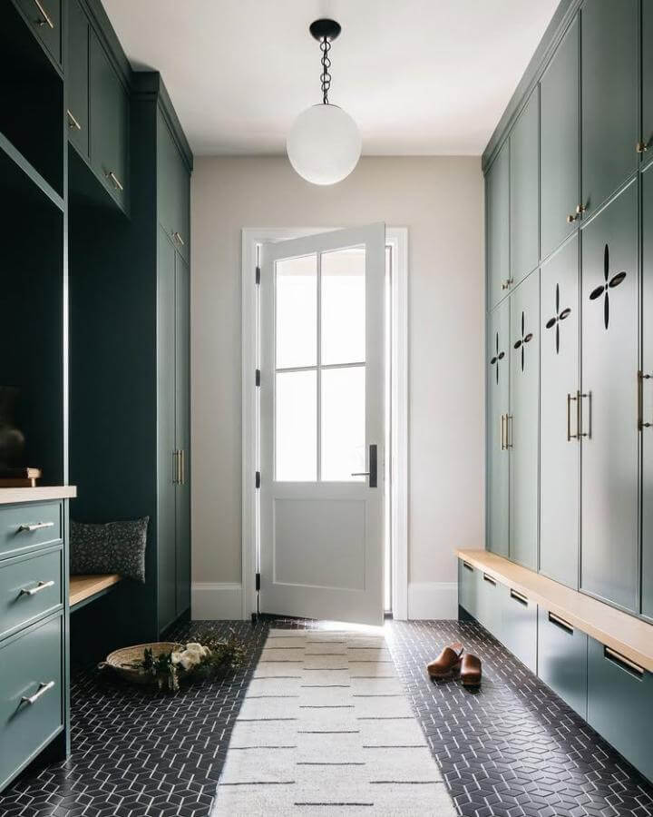 Deep green cabinetry with cutout accents and wood bench tops in a bright mudroom by @annaryadesign elegant and practical storage.