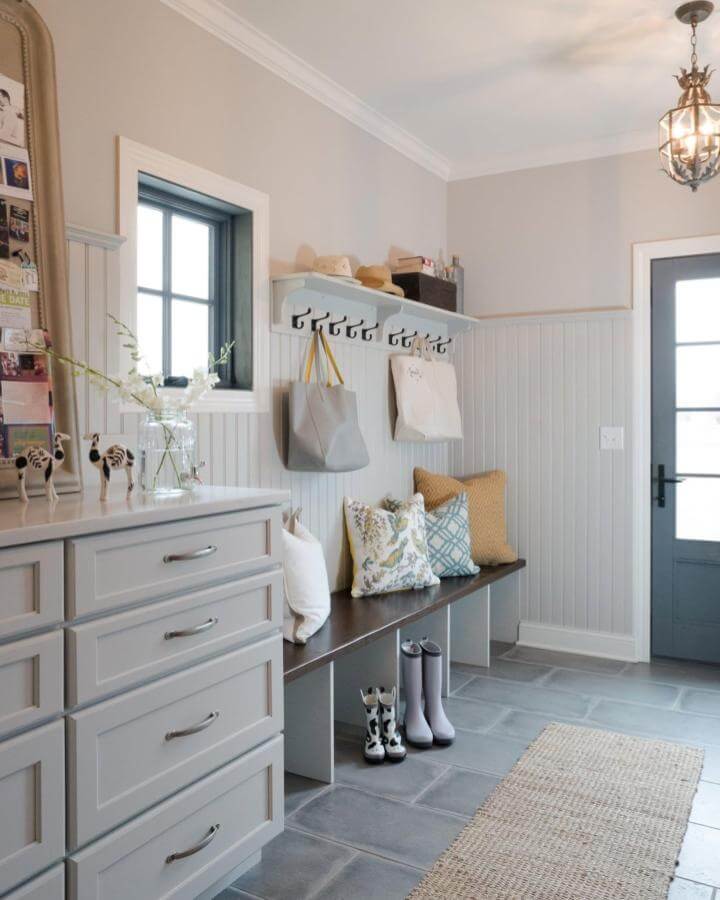 Light gray beadboard mudroom built ins ideas with dark wood bench, black hooks, and cozy cushions by @karrbick_design.
