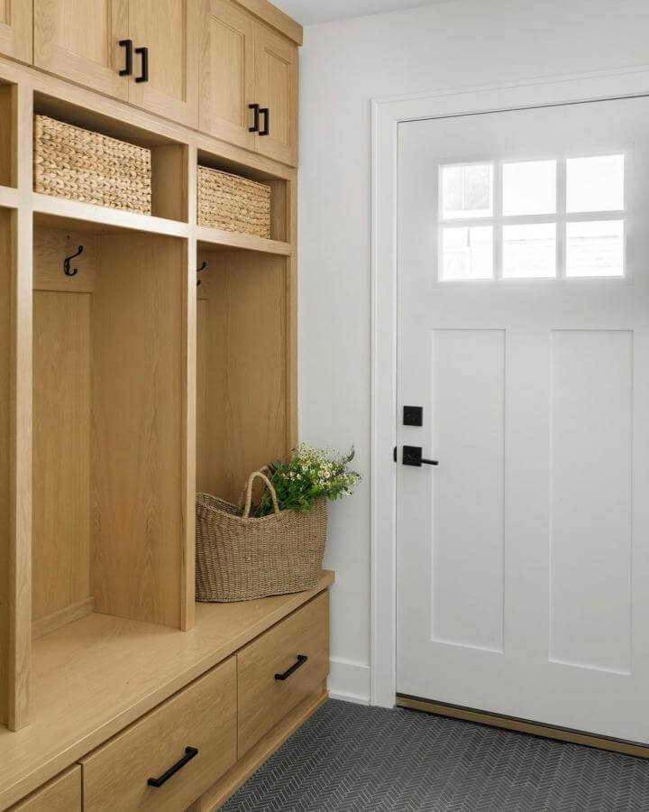 Natural oak built ins with woven baskets and black handles from @davisinteriorsmn in a bright, tidy entry space.