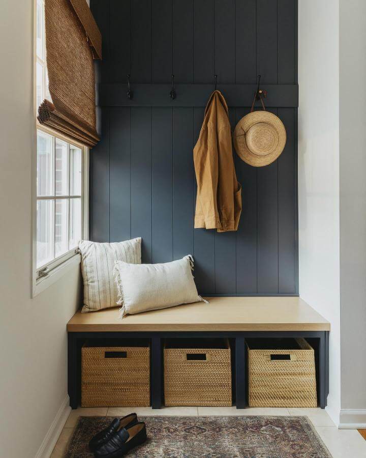 Navy shiplap wall with natural wood bench and woven storage baskets in a bright mudroom entryway