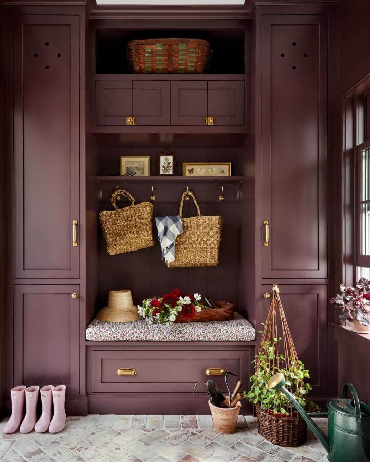 Plum built-in mudroom seating with wicker baskets and brass hooks from @jenniferbeekhunter brightened by floral cushion and rustic accents.