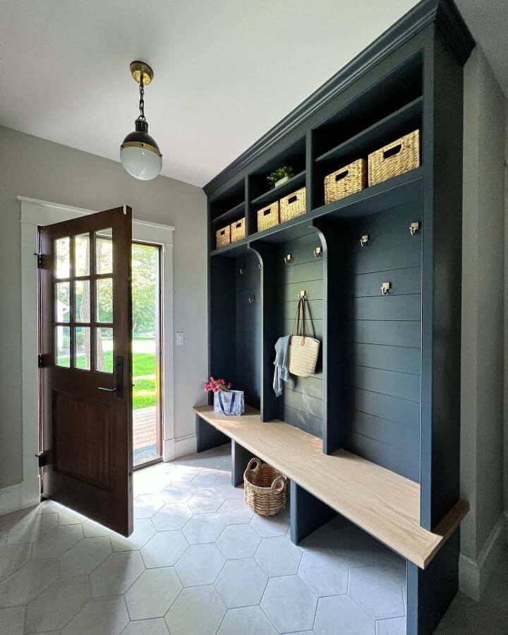 Deep navy built in bench with natural wood, brass hooks, and woven baskets in bright mudroom entryway by @muellerhomesinc