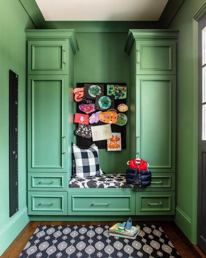 Green painted mudroom cabinetry with built in bench cushion and kids artwork from @kuohphotographyinteriors featuring black and white textiles.