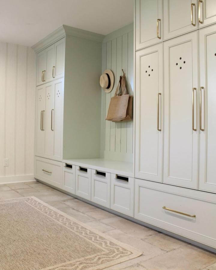 Soft sage green paneled mudroom built ins with brass handles and cubby seating from @olivehilldesigncompany. Functional and stylish storage solution.