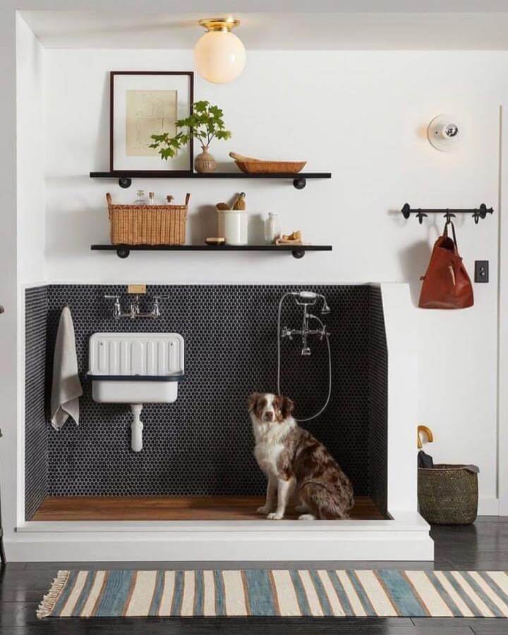 Black honeycomb tile mudroom dog wash space with white sink and wood shelves by @simplyuniquespace with brass fixtures and striped rug.