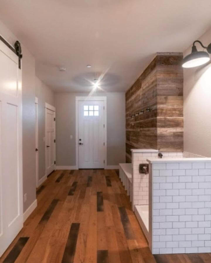 Wood plank textured wall and white tiled dog wash station with bench in mudroom space from @woodlandhomecompany.