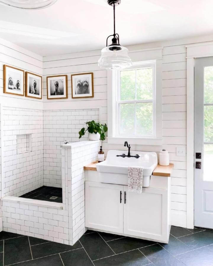 Bright white tiled dog wash station with black fixtures and wood countertop from @brunoandlibby. Black grout makes the space pop.