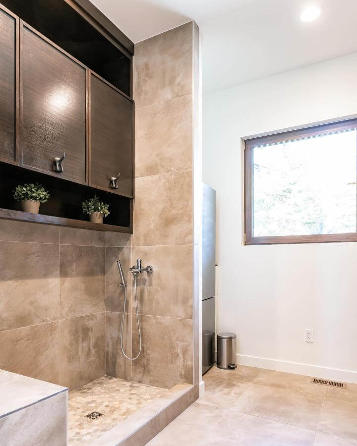 Neutral stone tile mudroom with dark wood cabinets and a handheld pet shower sprayer by @rebekahwestoverphotography. Stylish, practical dog bath area.