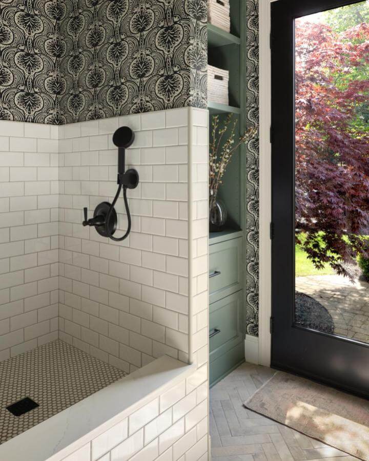White subway tile dog wash station with black fixtures in mudroom by @laurayeagersmith featuring patterned wallpaper and green cabinetry for mudroom dog wash ideas.